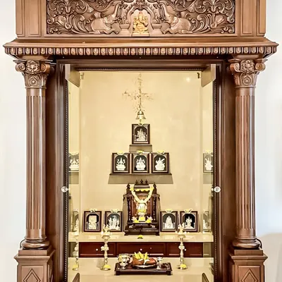 A traditional and ornate pooja mandir crafted from dark, intricately carved wood. The design features classical pillars and a detailed cornice, creating a grand and sacred temple-like structure within the home.