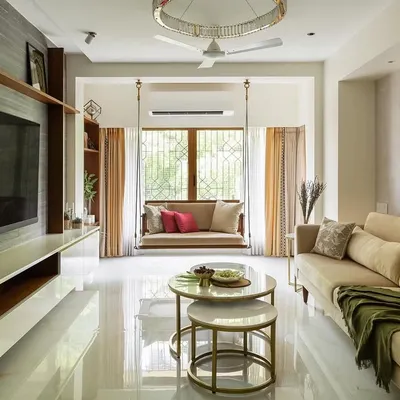 The living room of the Calm Abode, featuring a comfortable beige sofa, nested marble coffee tables, and a traditional wooden swing. The space is bathed in natural light, creating a warm and inviting atmosphere.