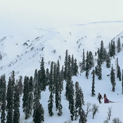 A breathtaking wide shot of a couple walking through the snow-covered landscapes of Kashmir. This is the kind of epic, cinematic pre-wedding photography we love to create.