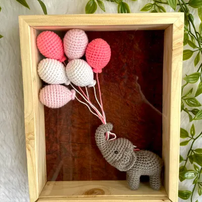 A gentle crochet elephant holding a bouquet of pink and white balloons, all set within a deep wooden frame. This 3D nursery wall art is perfect for a baby girl's room and can be personalized with her name.