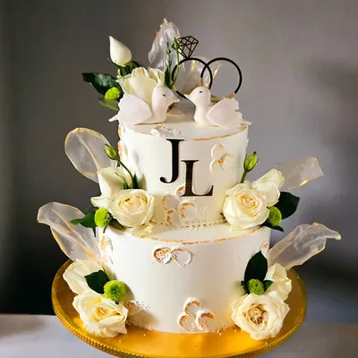 Pure elegance in white and gold. This two-tiered engagement cake is adorned with fresh white roses, delicate rice paper sails, and a pair of sweet, edible doves, symbolizing the couple's union.