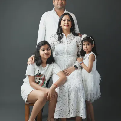 This is a classic family portrait from our Noida studio. We arranged this family of four, with parents and two daughters, for a timeless look against a simple grey backdrop, highlighting their connection and coordinated white outfits.