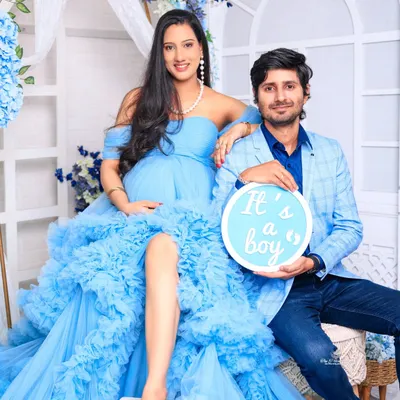 A classic couple's portrait celebrating the upcoming arrival. The mother-to-be is stunning in a ruffled blue gown, while her partner holds an "It's a boy" sign, sharing their joy.