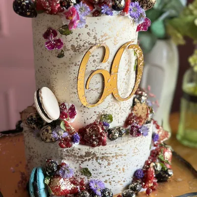 Berry tall, berry extra, berry delicious! This two-tiered cake for a 60th birthday is loaded with fresh berries, macarons, and edible flowers, all dusted with a touch of gold.