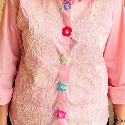 A row of my multi-colored crochet flower buttons sewn onto a pink shirt. This image shows how they add a pop of color and a playful, custom feel to an everyday garment.