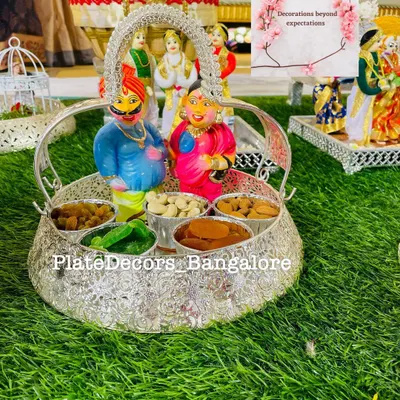 A traditional wedding platter with Marapachi Bommai (couple dolls) made from wood, placed in a silver basket filled with assorted dry fruits.