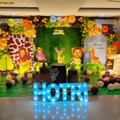 A grand safari-themed first birthday party setup. This decoration features a hedge wall, animal cutouts, a custom welcome sign, marquee letters, and an organic balloon arch in jungle-inspired colors.