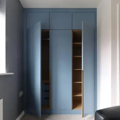 This floor-to-ceiling wardrobe in a matte blue finish features sleek, long handles and offers immense storage. The doors are open to reveal the custom interior with both hanging space and shelving.