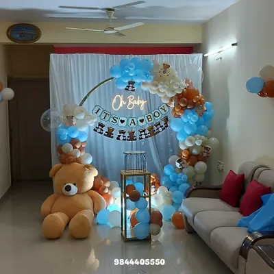 A full view of a teddy bear themed "It's a Boy" baby shower. This cozy home setup features a circular backdrop with a neon sign, a blue, brown, and white balloon arch, and a giant teddy bear.