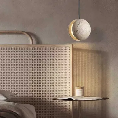 A beautiful pendant light made from natural stone, hanging as a bedside lamp. The light gives the stone a warm, moon-like glow, perfect for a serene bedroom.