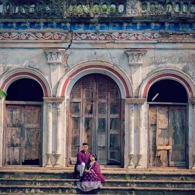 A couple dressed in traditional attire posing in front of a beautiful old haveli, giving the photo a royal and historic feel.
