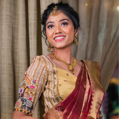 A smiling bride adorned in a masterpiece. This golden bridal blouse features incredibly detailed hand-embroidery, with motifs that tell a story, making her wedding day look truly one of a kind.
