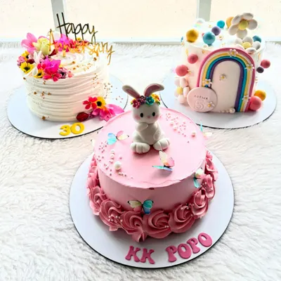 A trio of custom cakes, each with its own unique story. An elegant floral cake for an anniversary, a cute bunny cake for a child, and a rainbow cake for a 5th birthday.