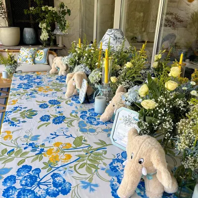 A beautifully set table for a baby's Mundan ceremony, featuring a blue and yellow floral tablecloth, plush elephant toys, and fresh flower arrangements.