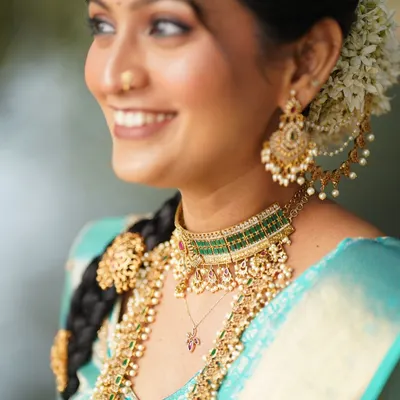 A beautiful close-up of a South Indian bridal look. This shot highlights the traditional braided hairstyle with gold accessories, the layered temple jewelry, and the soft, glowing makeup.