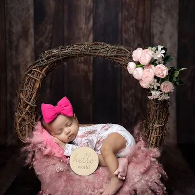 A perfect "Hello World" moment. This baby girl is sleeping peacefully in a rustic wreath basket, adorned with a bright pink bow and soft flowers.