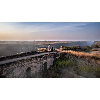 A cinematic drone shot of a couple during their pre-wedding session on an old stone bridge in Prayagraj. This high-angle view captures the vast landscape and the intimacy of the moment.