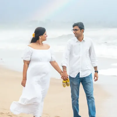 A beautiful walk along the shore, with a rainbow gracing the sky. This couple is holding hands, carrying tiny baby shoes, stepping towards their future.