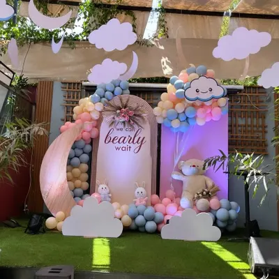 A dreamy "We Can Bearly Wait" baby shower theme. This outdoor setup features a pastel balloon arch, a large moon prop, and cute teddy bear and bunny figures.