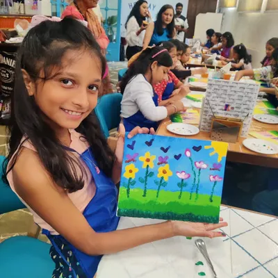 A young artist beaming with pride as she displays her finished floral canvas painting at Nishka's 10th birthday party.