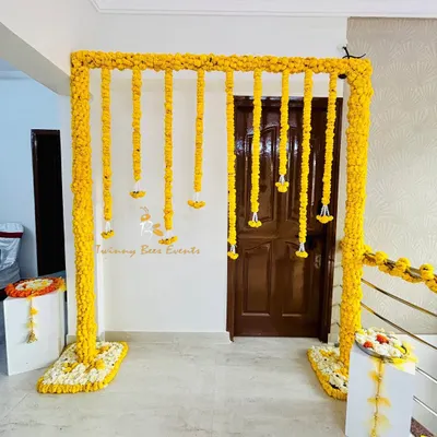 A classic Haldi decor setup featuring a square arch and hanging strings of bright yellow marigolds. This simple and elegant backdrop is perfect for intimate ceremonies at home.
