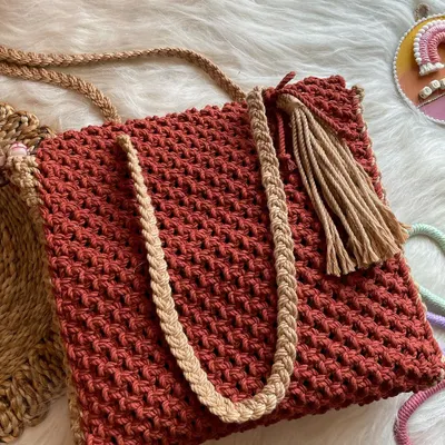 This roomy tote bag in a rich rust color is perfect for everyday use. It features contrasting tan braided straps and a stylish side tassel for a touch of boho flair.