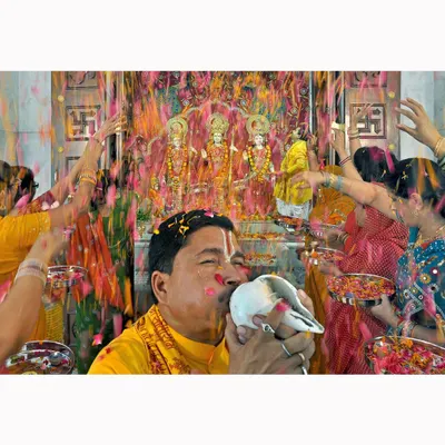 A priest blows a conch shell during a temple ceremony, showered with flower petals. This image was part of a commissioned project and captures the sensory richness and devotion of the celebration.