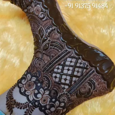 This is a full bridal foot design with the henna paste still on. The design features a combination of floral bands and a central grid pattern, covering the foot for a traditional look.