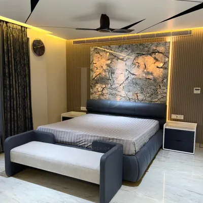 A complete view of a master bedroom I designed. It features a custom bed with a leather headboard, a matching bench, and sleek bedside tables, all set against a dramatic, back-lit marble-effect wall.