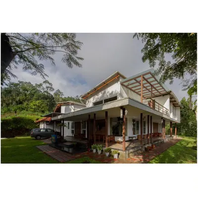 A wide-angle view of the 'Malenadu Mane', showing how the structure with its extended verandahs and sloping roofs sits comfortably within the green canopy of the surrounding coffee plantation.
