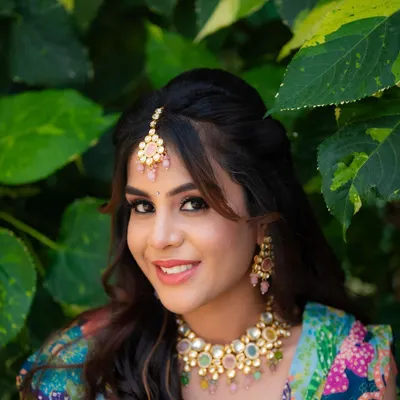 A perfect Mehendi portrait. The bride's happy smile, colorful jewelry, and the lush green background come together to create a fresh and joyful image.