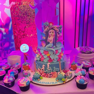 A full view of the mermaid-themed dessert table I created for a magical birthday party. The centerpiece is a two-tier cake with a mermaid topper, surrounded by coordinating cupcakes and other themed treats.