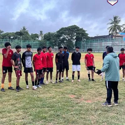 A coach provides tactical instructions to a group of our youth players during a daytime training session on the grass pitch.