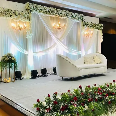 A luxurious engagement stage with flowing white drapes, elegant chandeliers, and a comfortable chaise lounge for the couple. The stage is lined with red and white floral arrangements, adding a touch of romance.