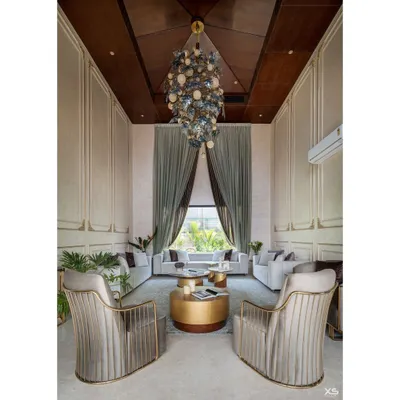 The living room of this luxury villa in Bengaluru features a 22-foot ceiling and a dramatic wooden gable roof. We designed the space with plush, neutral-toned furniture and a massive custom chandelier to create a feeling of royal comfort.