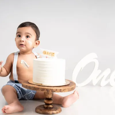 The moment of anticipation just before the cake smash begins. This simple and clean first birthday setup captures the curiosity of a one-year-old with a classic white cake and suspenders.