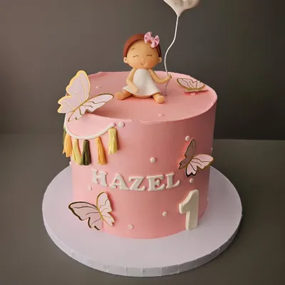 A pretty pink cake for baby Hazel's first birthday. This cake features a cute, hand-sculpted baby figurine holding a heart balloon, surrounded by delicate butterflies.
