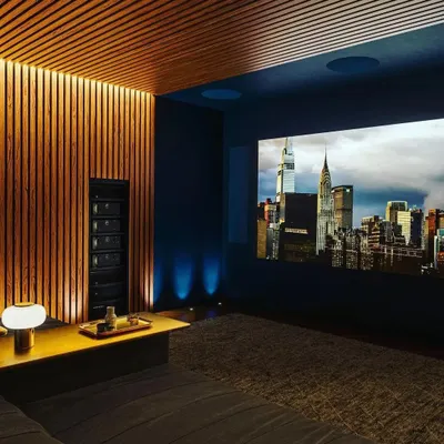 A modern and sophisticated home cinema featuring warm wood acoustic paneling and a dark color palette to minimize light reflection. The setup is powered by a Marantz AV receiver, driving a powerful in-wall and in-ceiling speaker system for a clean, high-performance result.