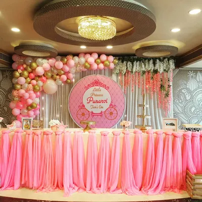 This is the main stage I created for Little Princess Punarvi's first birthday. The setup is defined by a beautifully draped pink table skirt, a custom backdrop with a princess carriage motif, and a cascading balloon arch with pink, white, and gold balloons.