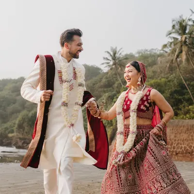 A candid shot of the couple laughing and running hand-in-hand on a Goa beach, perfectly capturing their joyful spirit in their wedding attire.