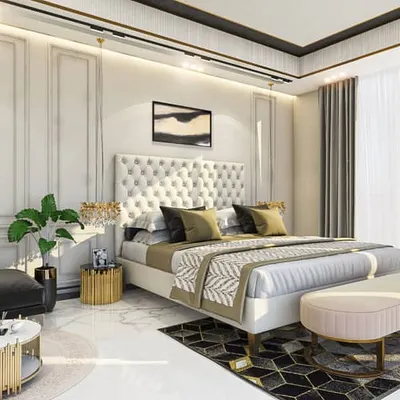 A bright and luxurious master bedroom featuring classic design elements. The tufted, full-height headboard and traditional wall mouldings are paired with modern gold accents and a marble floor for a timeless, hotel-like feel.
