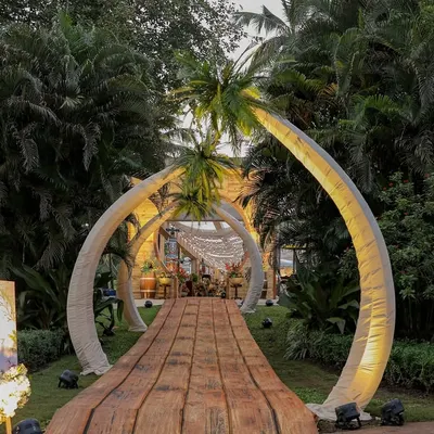 The grand entrance to our 'Bora Bora' themed event. A wooden boardwalk is framed by two massive, curved structures resembling palm trees, creating a dramatic and immersive welcome into our tropical world.