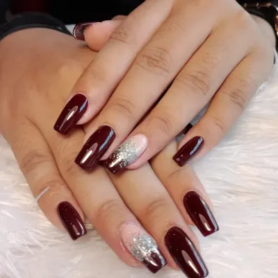A rich, glossy burgundy polish on long, square-shaped nails. The look is elevated with two accent nails featuring a silver glitter gradient over a nude base, creating a perfect balance of bold color and sparkle.