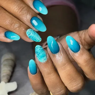 These stunning ocean ombré nails were created for a client's vacation. I blended layers of blue, turquoise, and seafoam shades to capture the look of waves, adding a textured shell effect accent nail for the perfect beach-ready look.