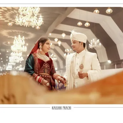 A classic wedding portrait of the couple, Kaushik and Prachi, holding hands after the ceremony. The grand chandeliers and warm lighting of the venue create a regal and timeless backdrop for this beautiful moment.