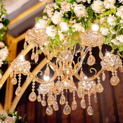 A close-up of pure opulence. A crystal chandelier hangs amidst a lush arrangement of white flowers, a detail that adds glamour and sophistication to any stage or mandap.