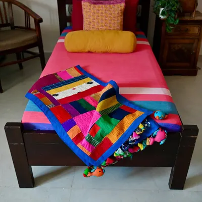 A full view of the improv quilt, a vibrant tapestry made entirely from fabric scraps and studio waste. The playful fish-shaped tassels are also crafted from leftover bits of cloth.