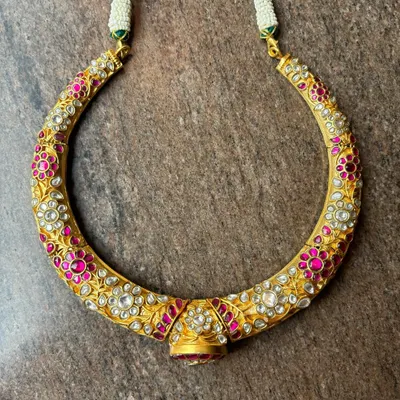 A unique and antique-style hasli necklace. This piece is crafted from silver with a gold-plated finish and is intricately adorned with pink and white Kundan stones for a rich, floral look.