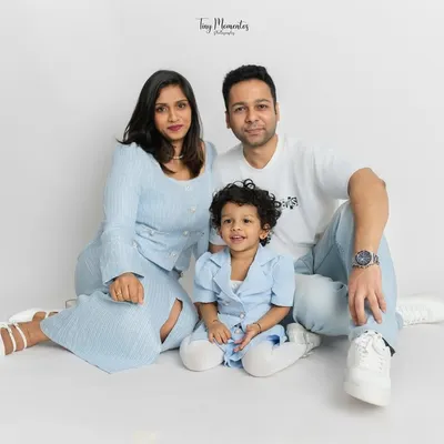 A classic family portrait with everyone looking towards the camera. The coordinated blue and white outfits create a serene and unified look against the minimalist white studio background.