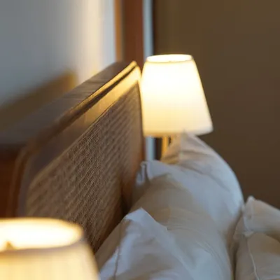 A detail of a rattan headboard glowing in the warm light of a bedside lamp, a moment of 'Rattan Grace'.